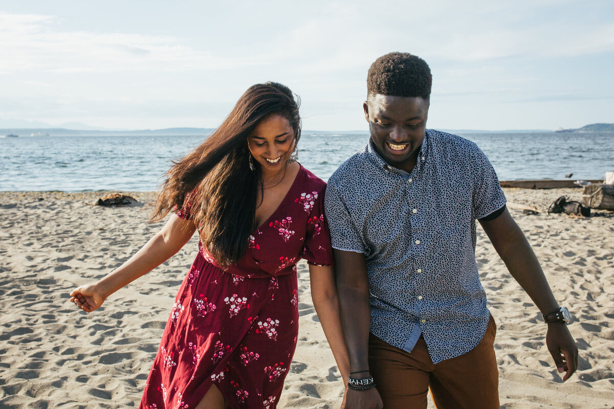 An engaged couple walking on a beach in Seattle
