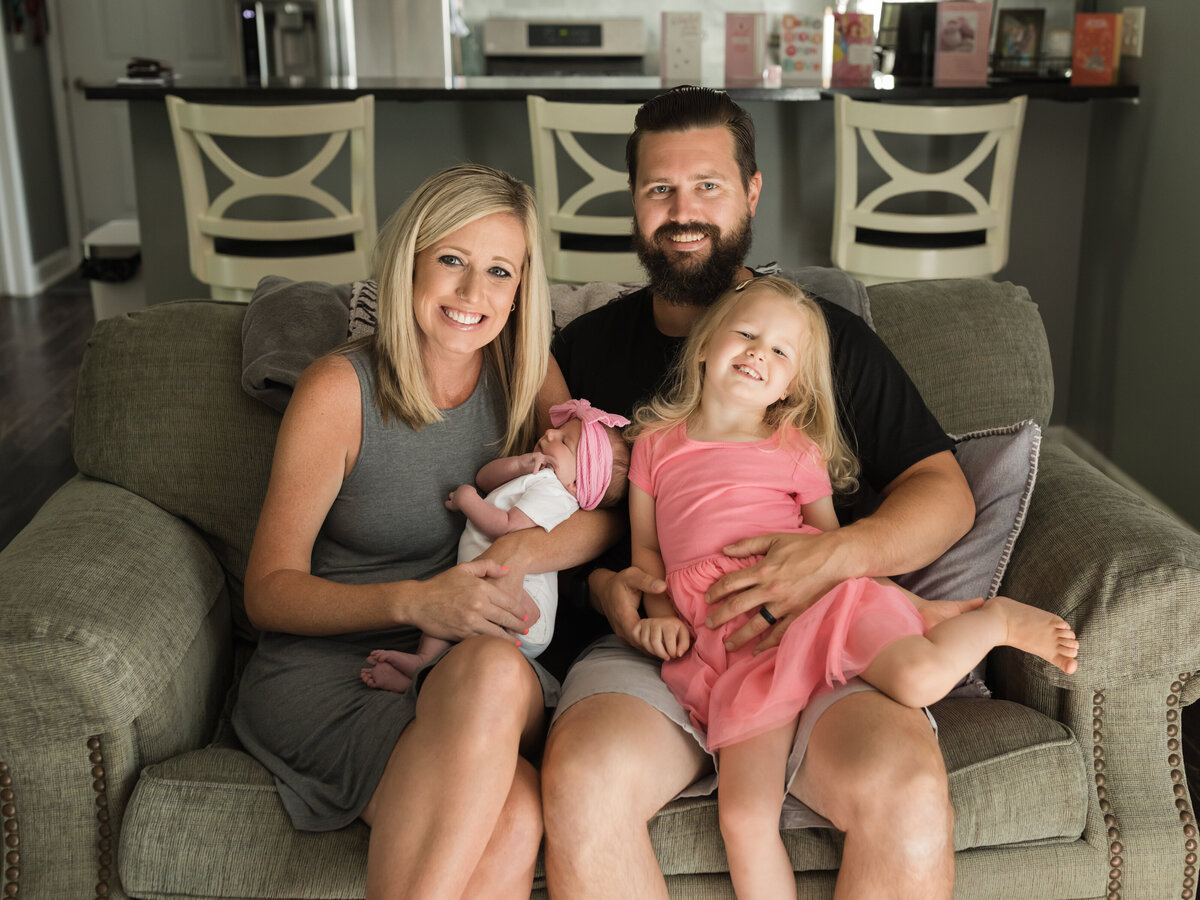 mom, dad, sister and newborn baby girl sitting on couch for in home session