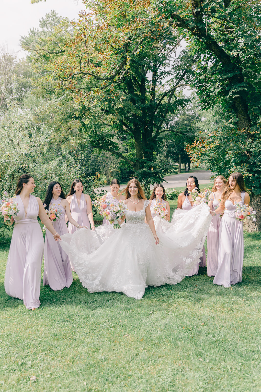 A bride and her bridesmaids hold pastel flower bouquets in the garden of the Forest and Stream Club.