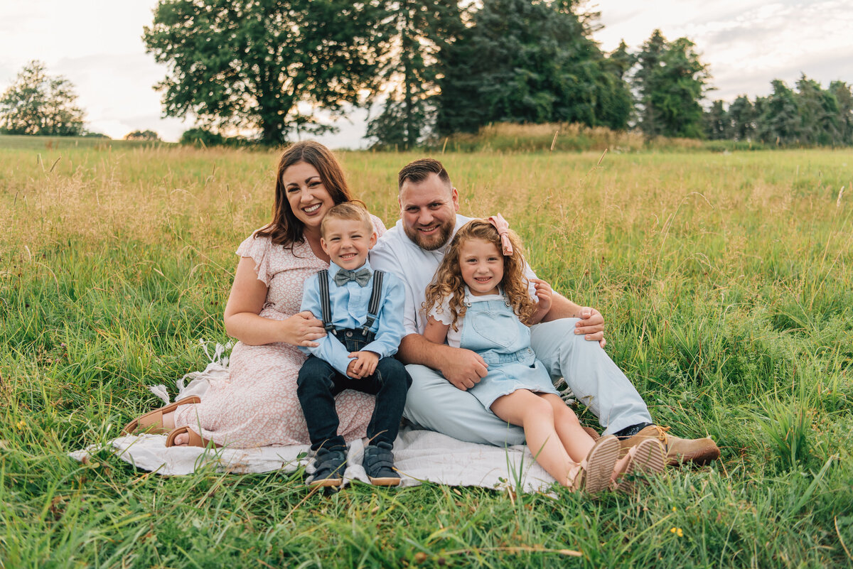 Family of four smiling on blanket in field