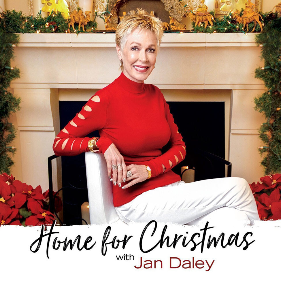 Album Cover Los Angeles Title Home For Christmas Artist Jan Daley sitting on white chair in front of decorated fireplace wearing red sweater