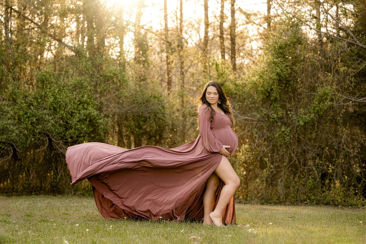 expectant mother dressed in a mauve dress poses with the dress train blowing in the wind