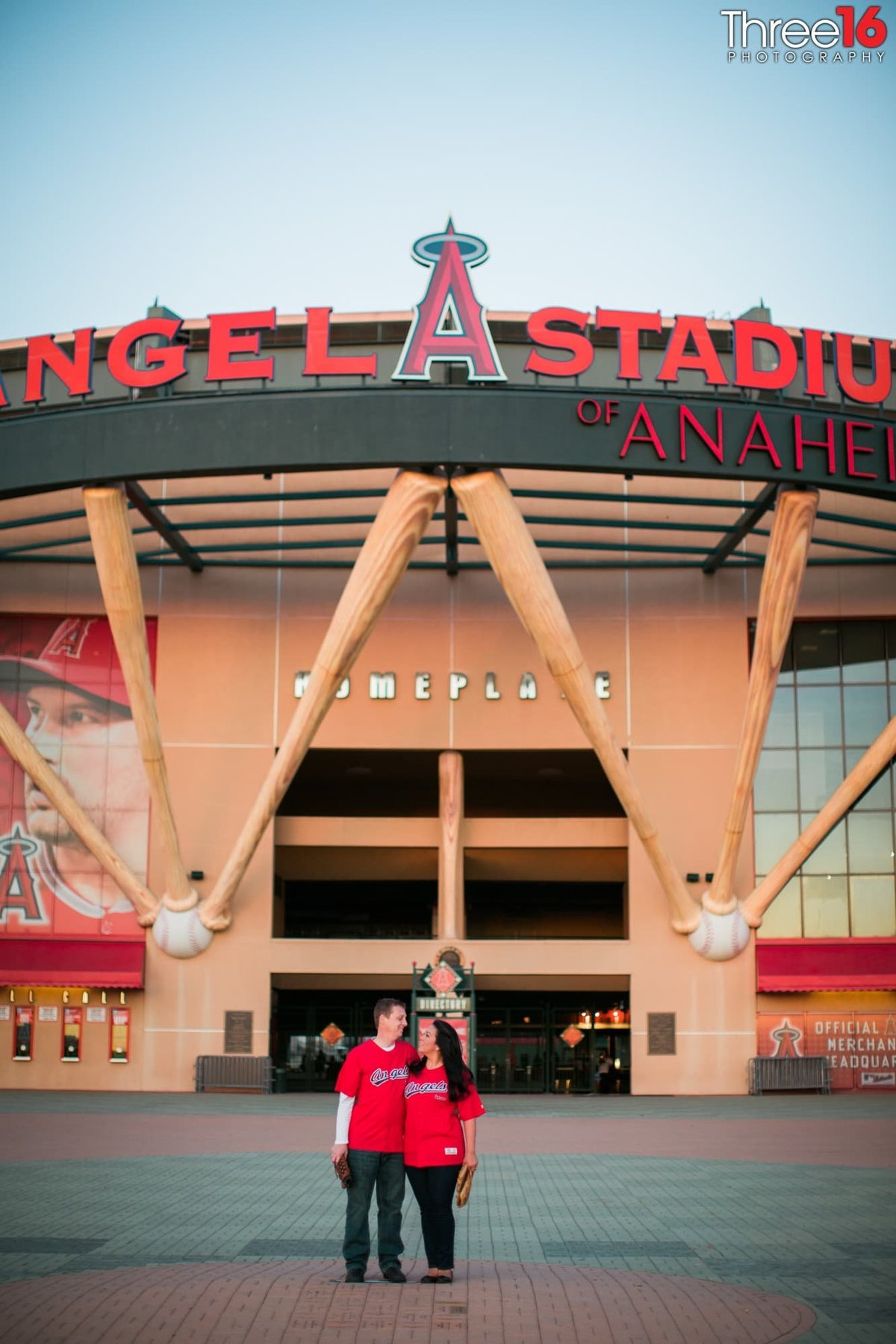 Engaged couple pose for engagement photos in front of Angel Stadium under the giant bats