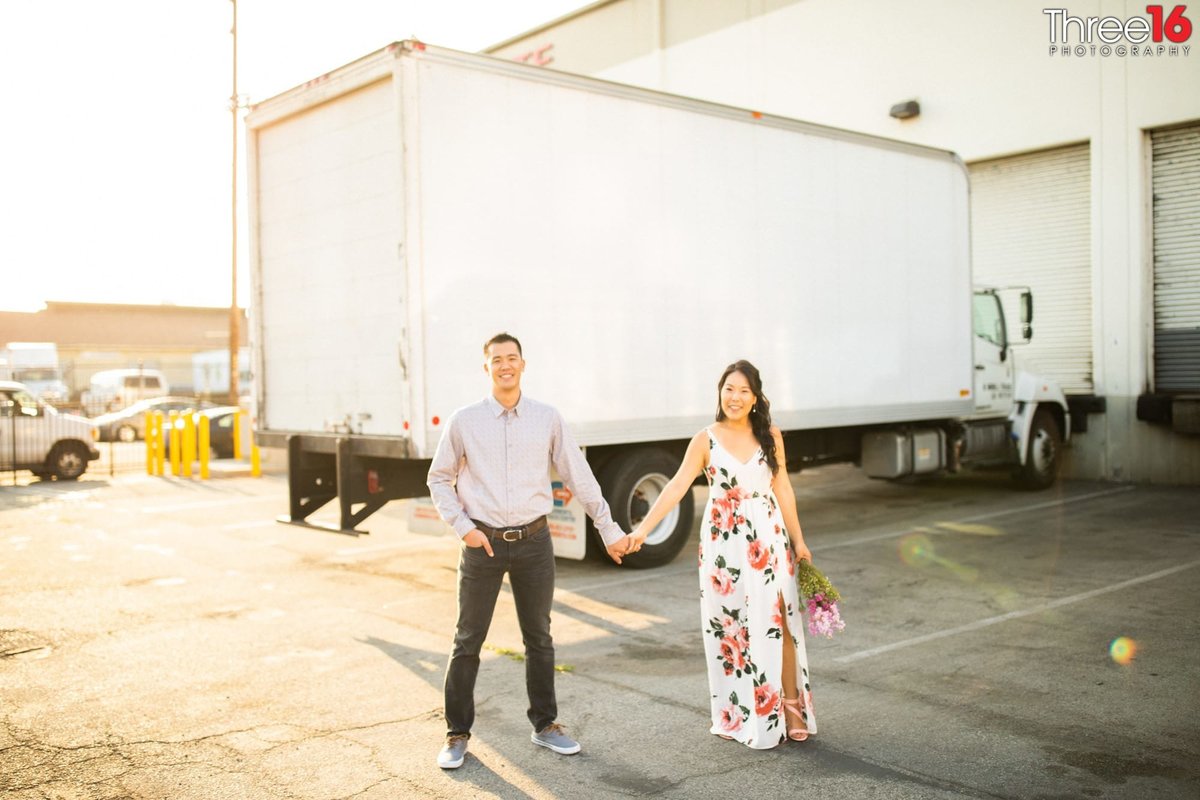 Engaged couple hold hands behind a warehouse