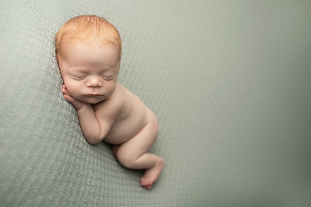 Close-up of a newborn boy with bright red hair, wrapped in a soft, neutral-colored blanket