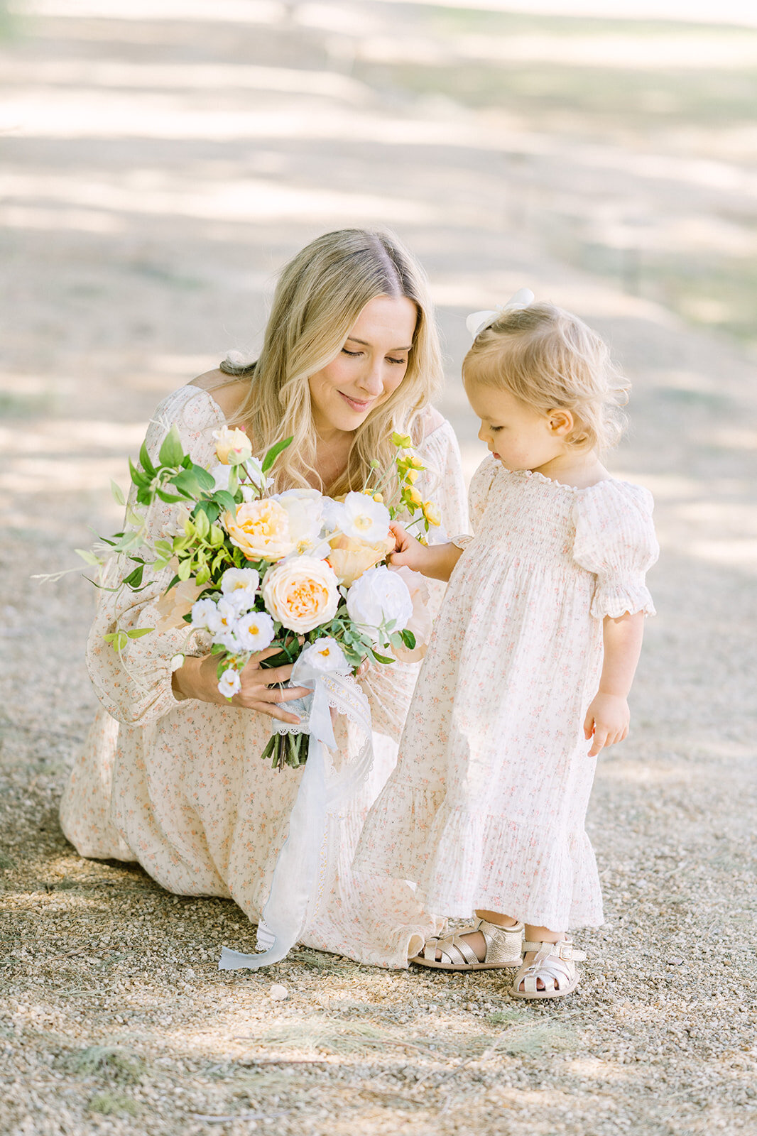 Mom and baby dressed in matching dresses admire a peach colored bouquet.