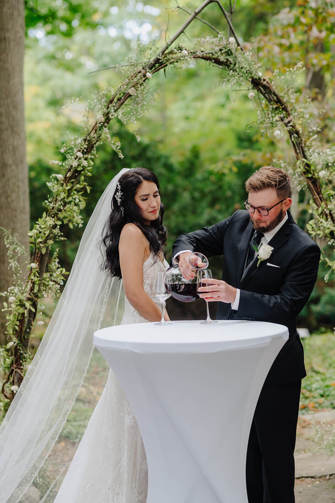 Groom pouring wine into a glass at forest wedding, Finger Lakes wedding, NY