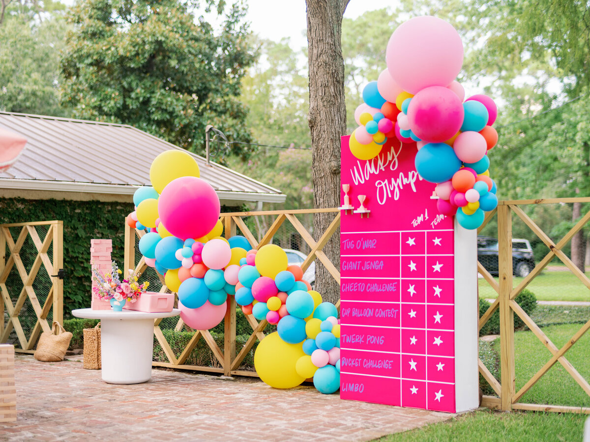 Pink, yellow and blue scoreboard backdrop design with balloon arches for a wacky olympics party