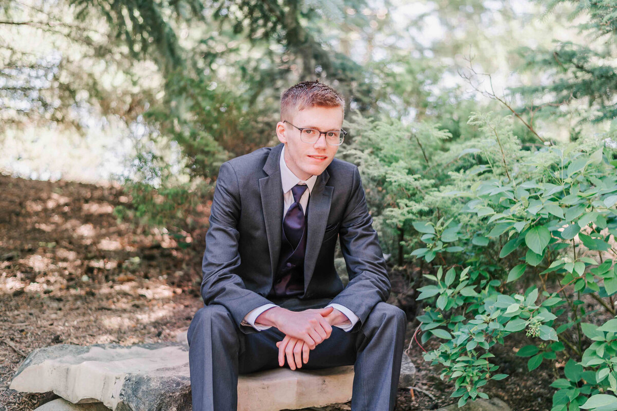 Sitting on a rock with his elbows on his knees. 