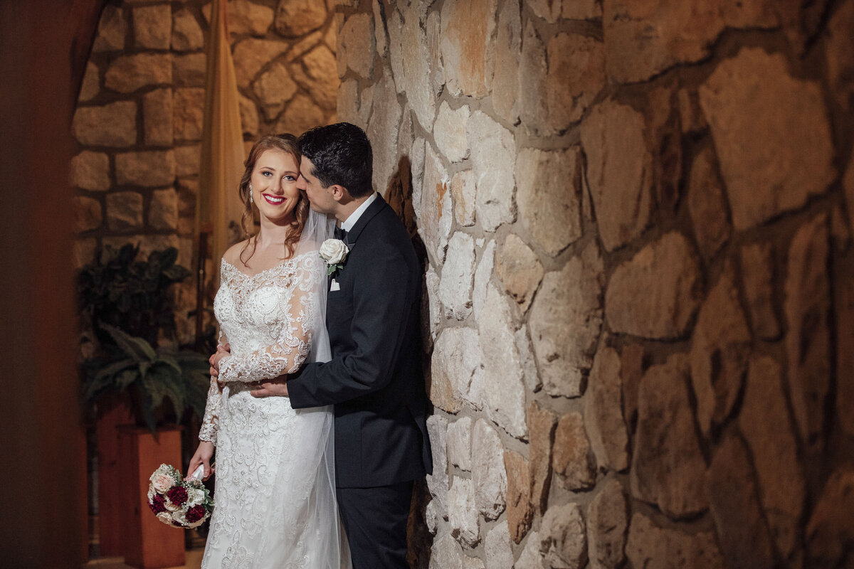 St. Frances Cabrini Church Wedding | Bride and Groom Embracing with Flowers by Stone Wall | Fairless Hills, Pennsylvania Photography