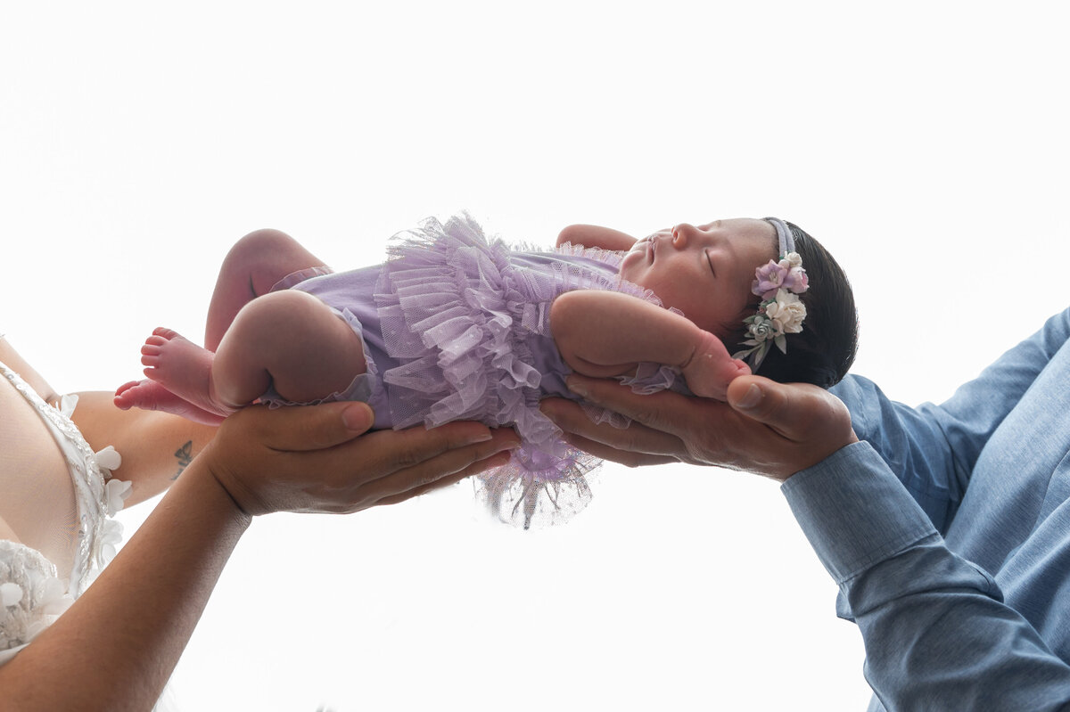 Newborn baby lying on her back, gently held in the air by a woman and man.