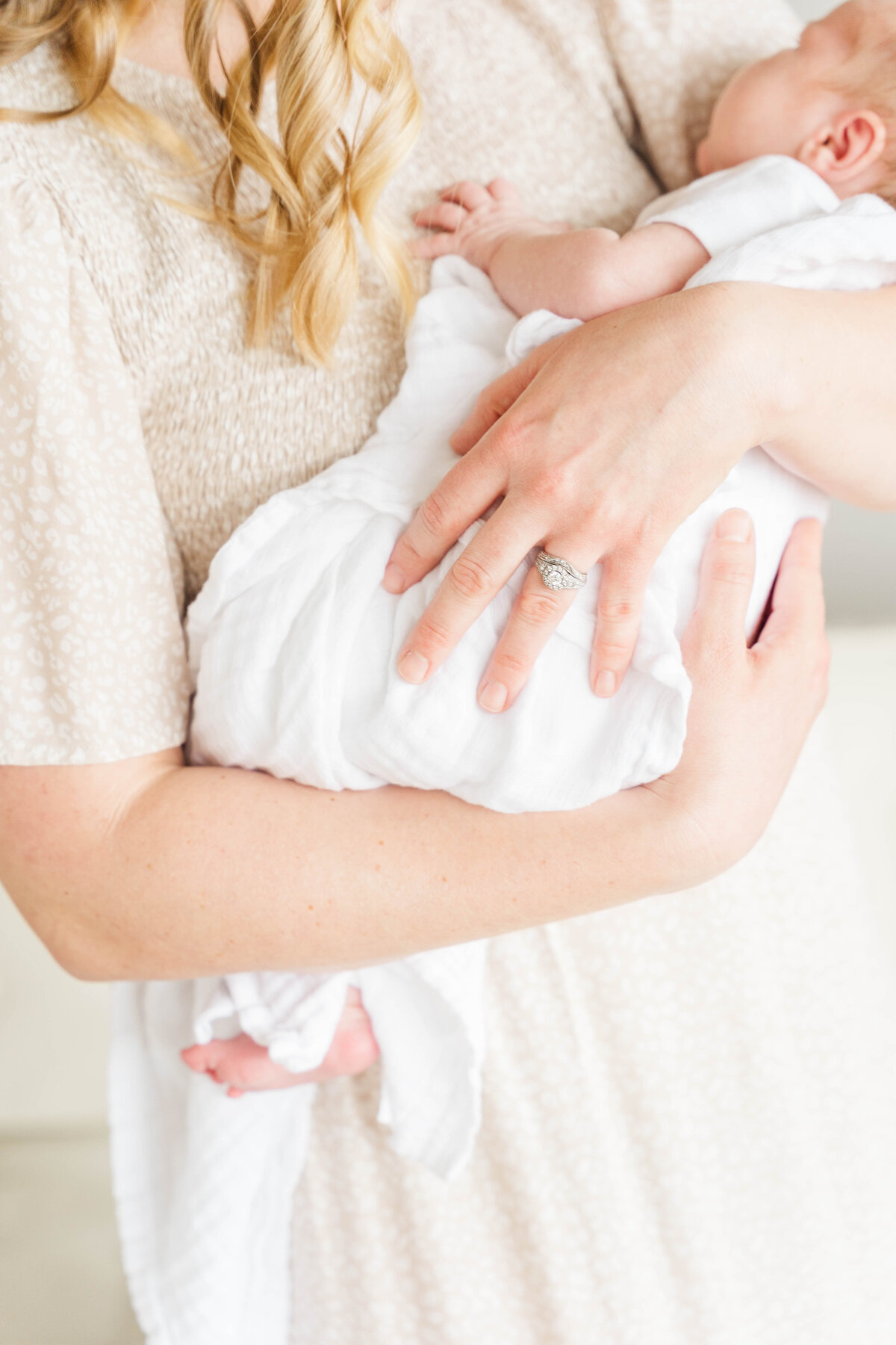 a mother holds her swaddled newborn in soft fabrics