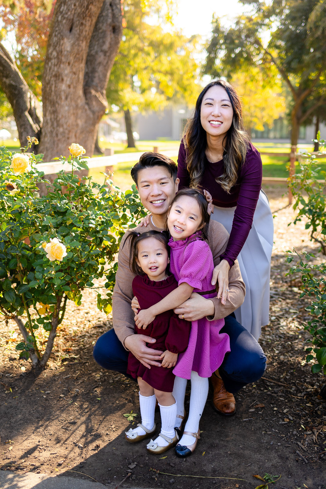 Parents kneeling with two young daughters by yellow roses at a Burlingame garden – Ellobelle Photography