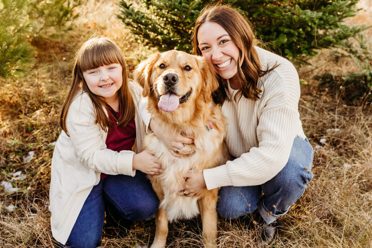 Two sisters wrapping their arms around their dog during their family portrait session.