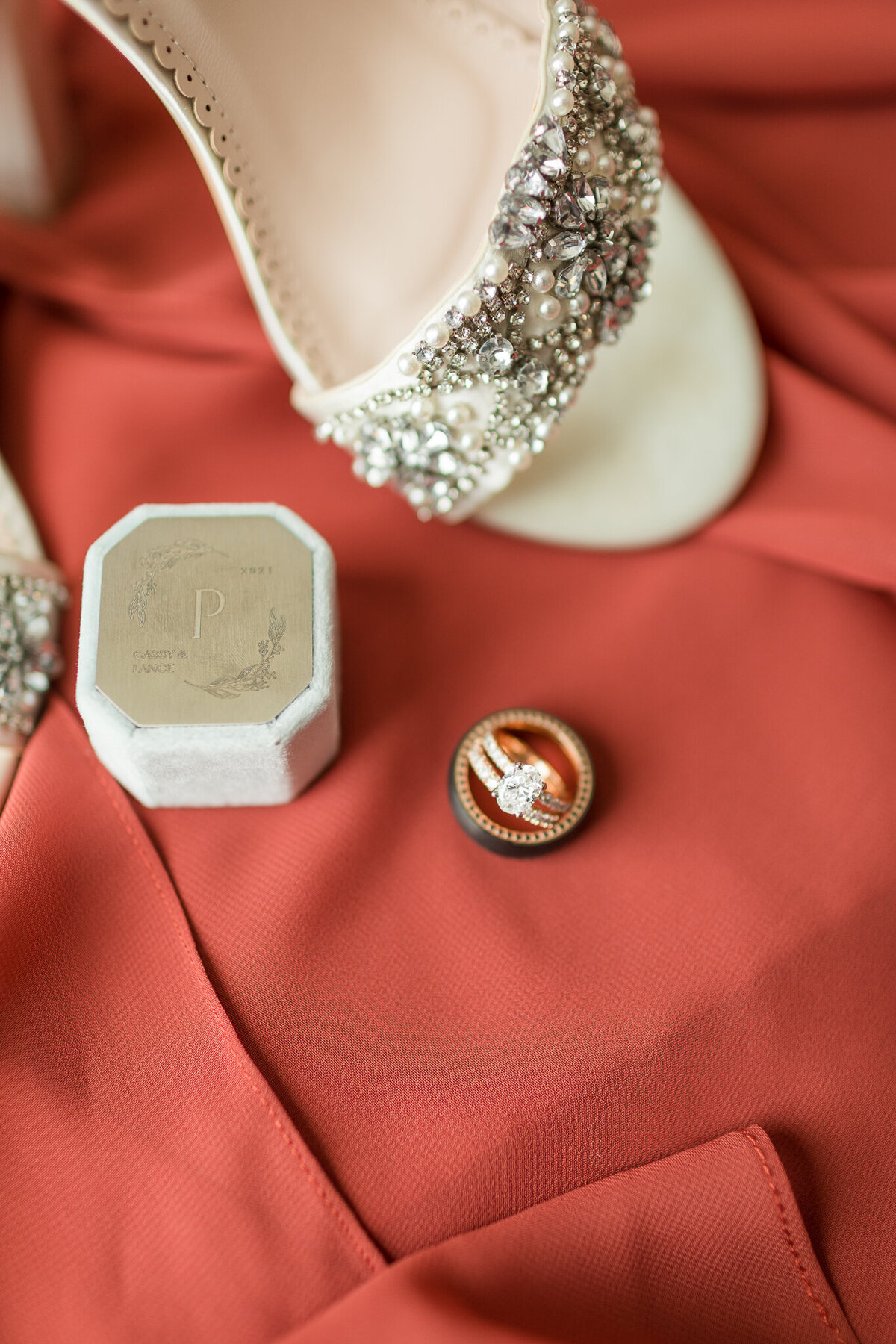 FLAT LAY CLOSE UP SHOT OF BADGLEY MISCHKA BRIDAL SHOES AND A PERSONALIZED DUSTY BLUE RING NBOX WITH A N OVAL CUT ROSE GOLD WEDDING RING SET