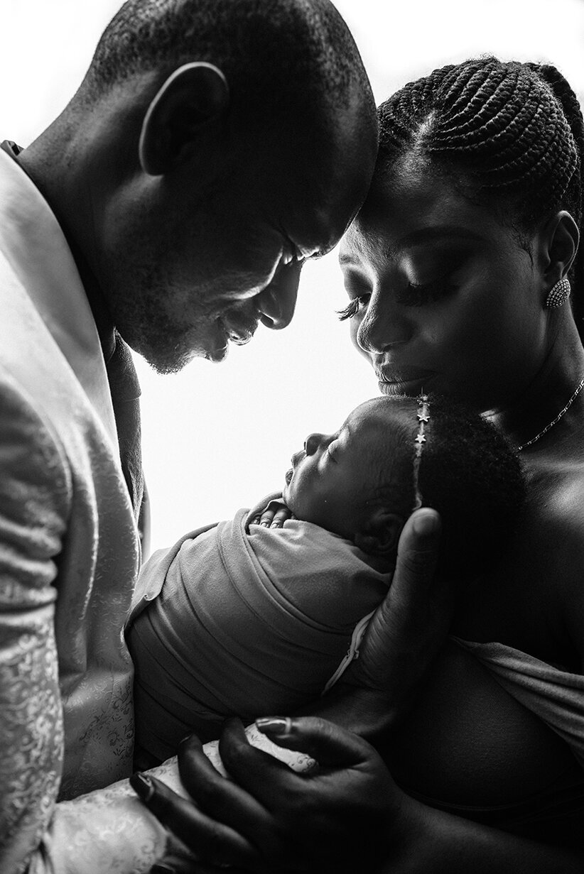 Black and white backlit photo of couple holding newborn daughter