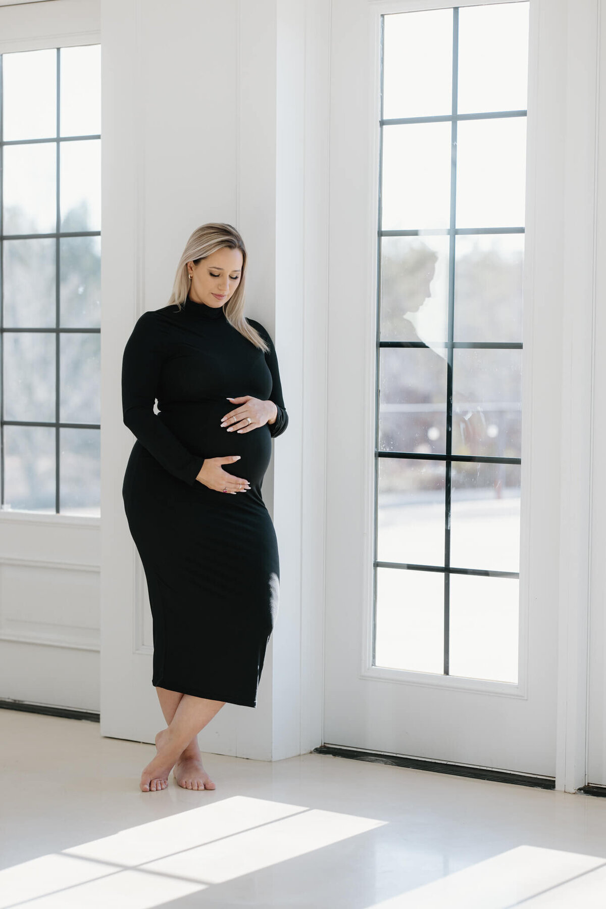 expecting mother in long black dress standing by a window at The Claremore in Tyler, TX