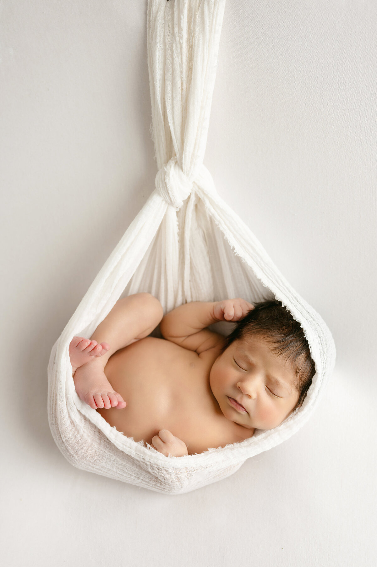 A unique newborn photography session in Pittsburgh, PA featuring a newborn baby peacefully resting in fabric. The creative setup adds a whimsical touch to this serene portrait, capturing the peacefulness of the newborn.