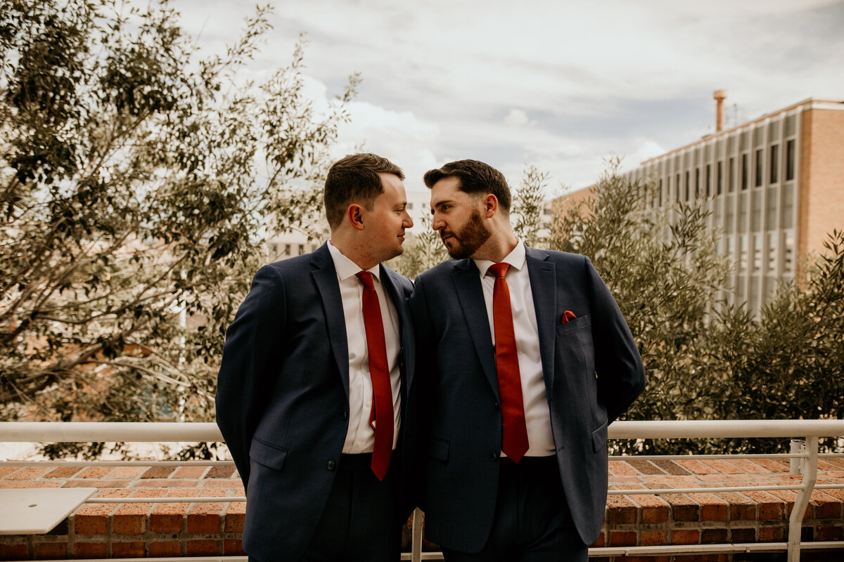 two grooms standing on a balcony in downtown Albuquerque about to kiss