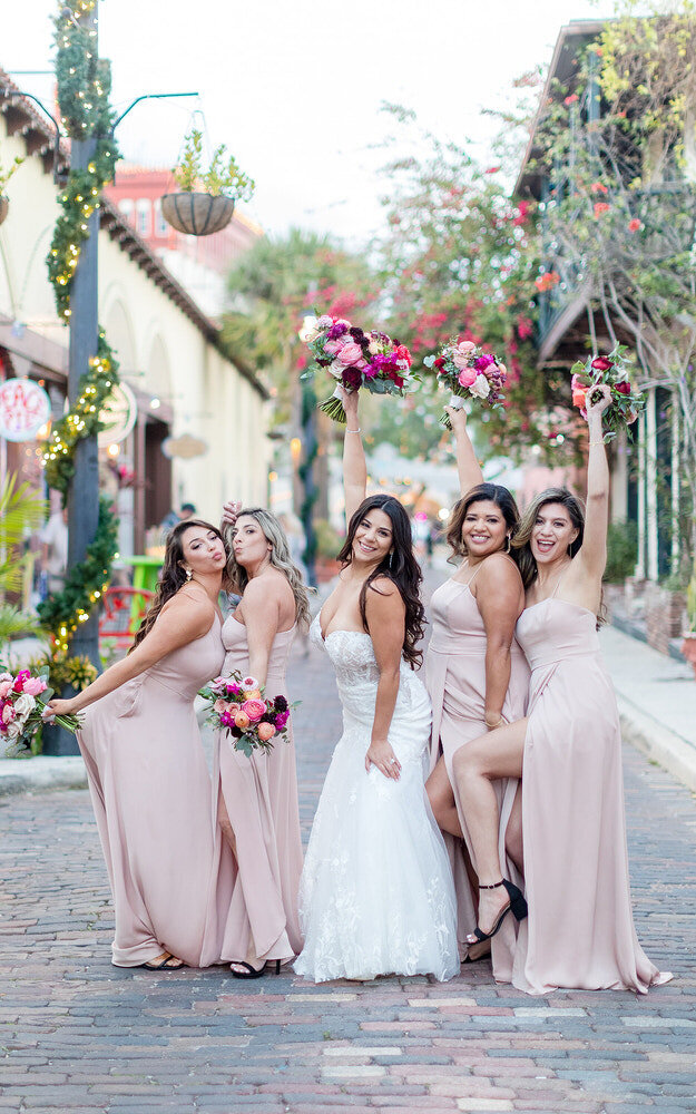 Classic bright and airy playful photo of bride and bridesmaids at a downtown St Augustine cobblestone street during a wedding