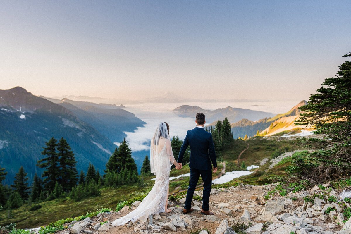 couple walking on the top of a mountain over looking a cloud inversion during their Washington Elopement