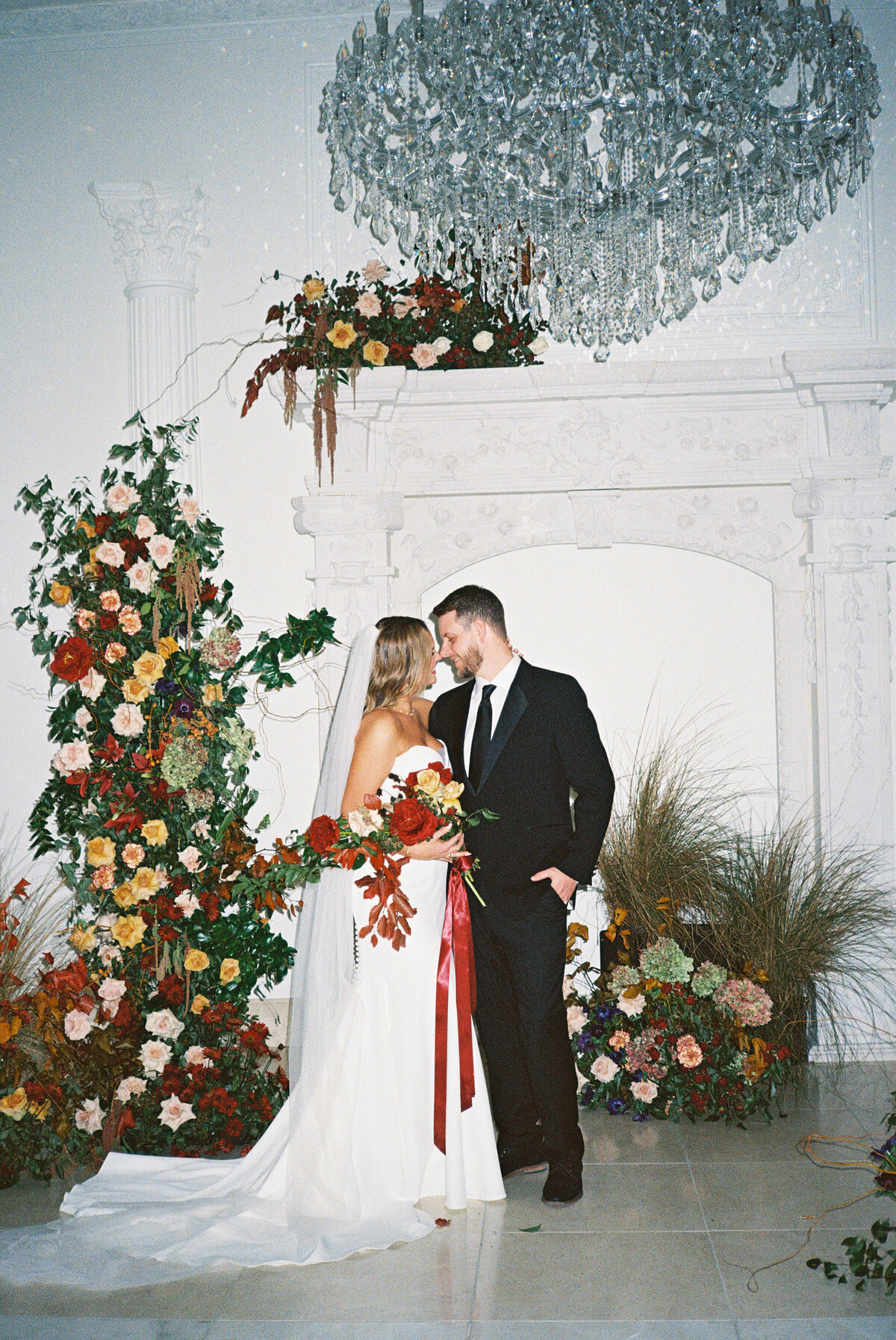 elaborate floral arch at wedding ceremony with bride and groom in black suit