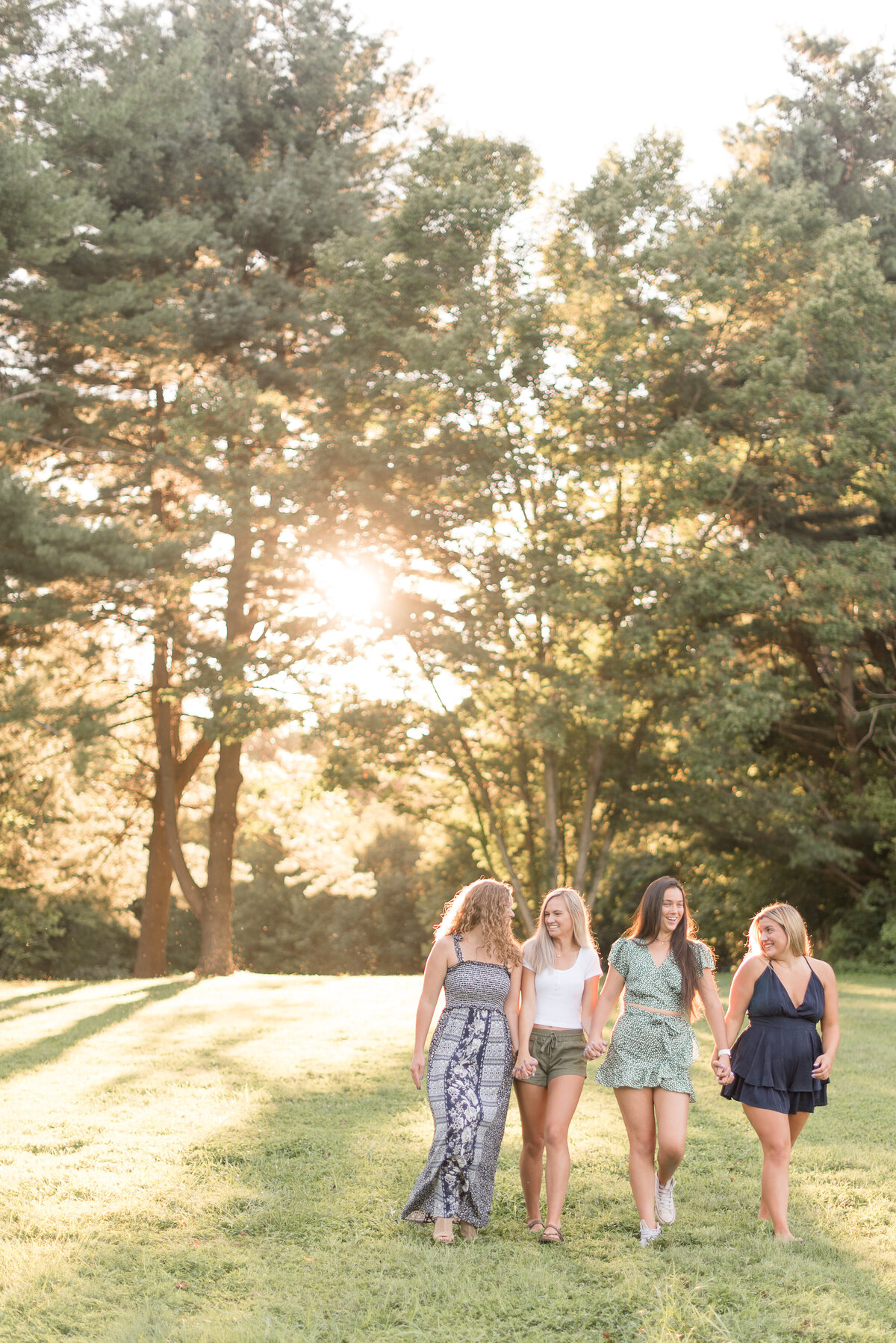 Four Senior girls holding hands walking towards camera with sun shining through trees behind them at Lancaster County Park.