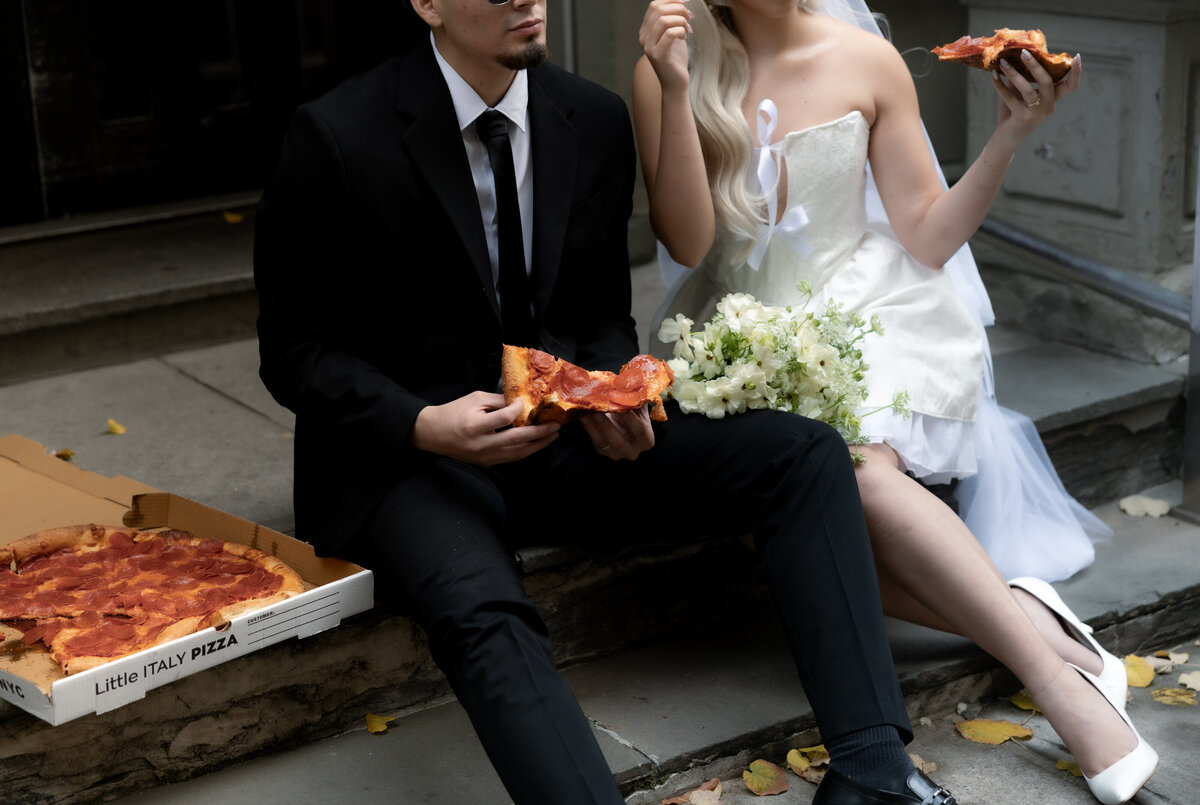 Bride and groom sharing a romantic moment while splitting a slice of pizza in NYC.