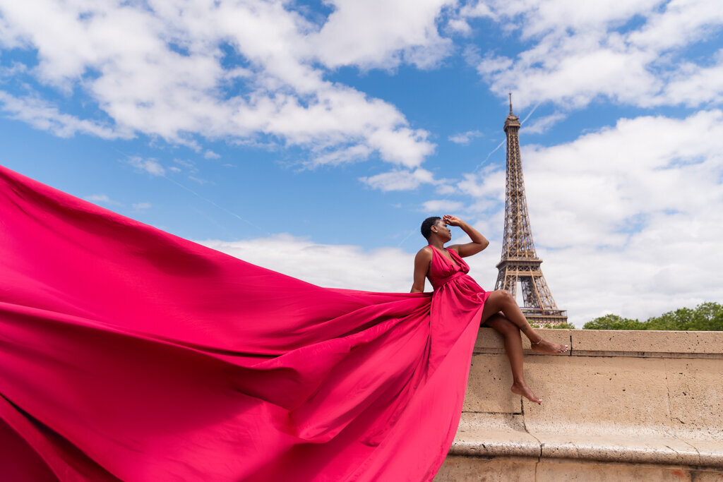 Elegant Paris portrait with woman seated on wall in flowing pink dress overlooking Eiffel Tower