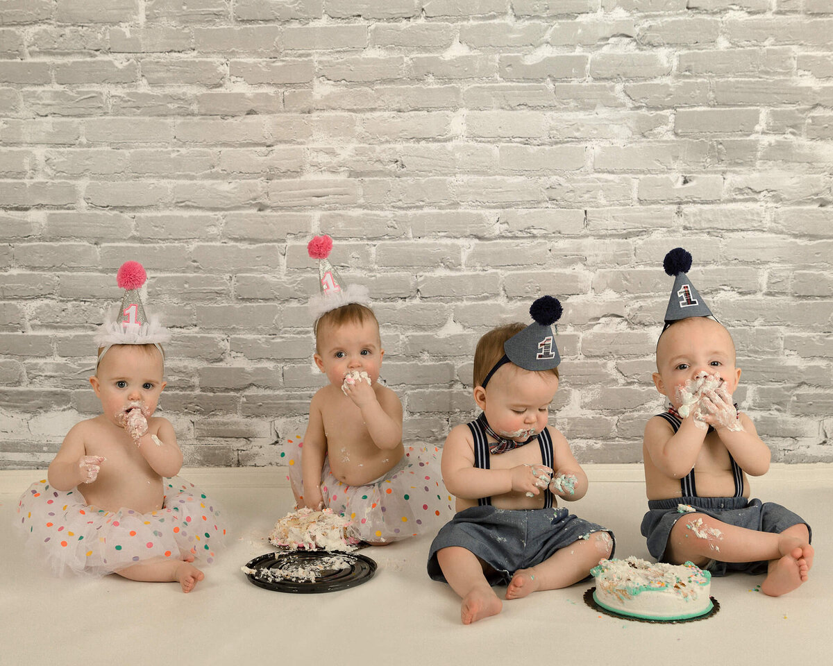 Quadruplets eating cake for the 1 year old cake smash. They are loving the cake and making a big mess.