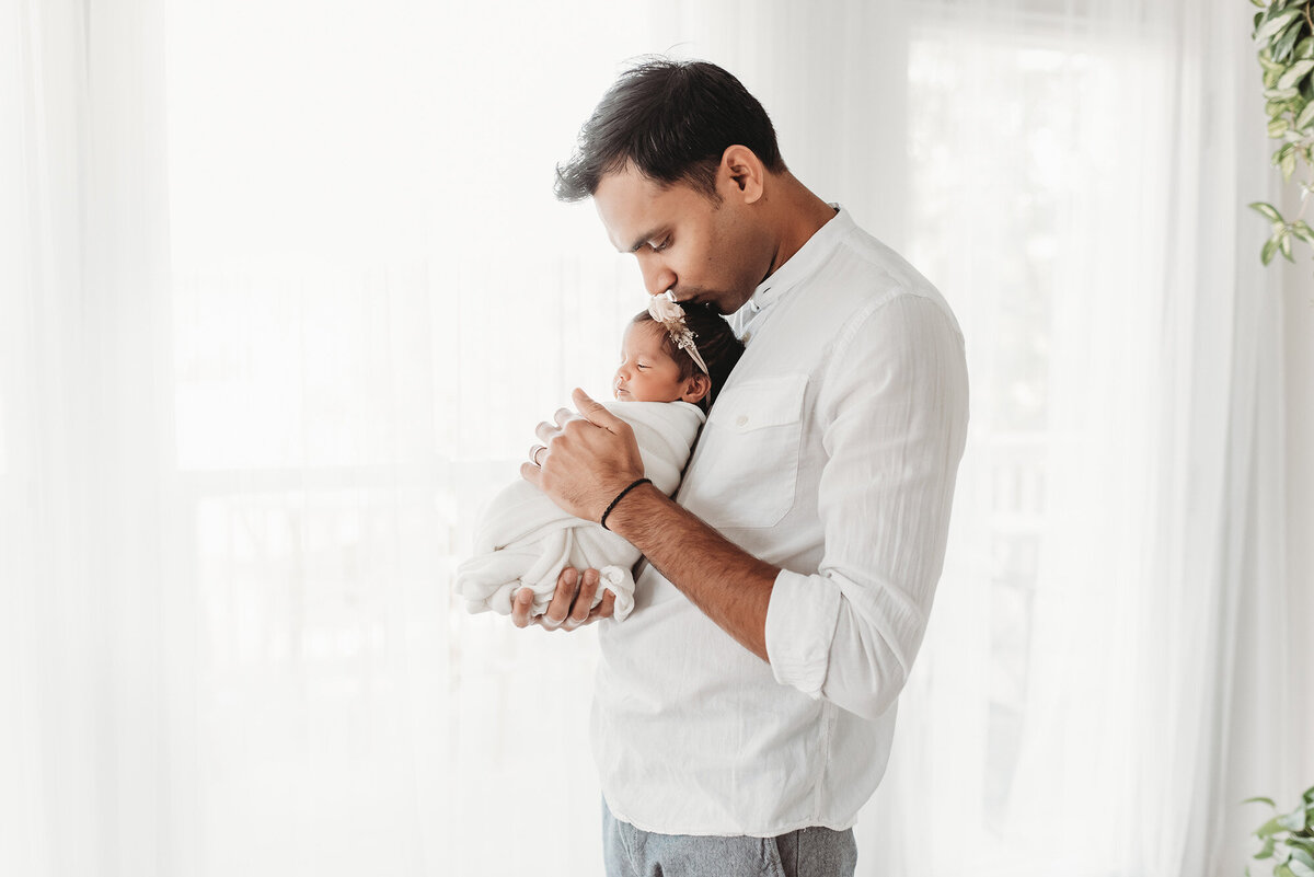 side profile of dad holding newborn girl on his chest and kissing her head