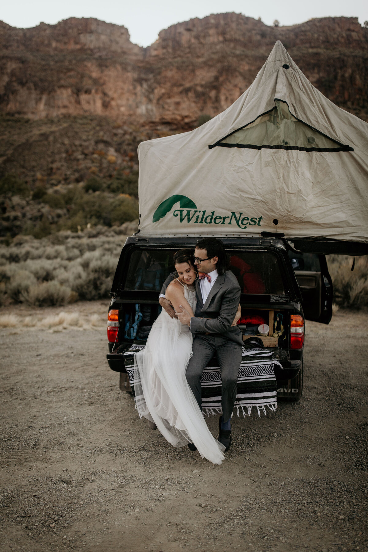 bride and groom sitting on a truck with a tent on top