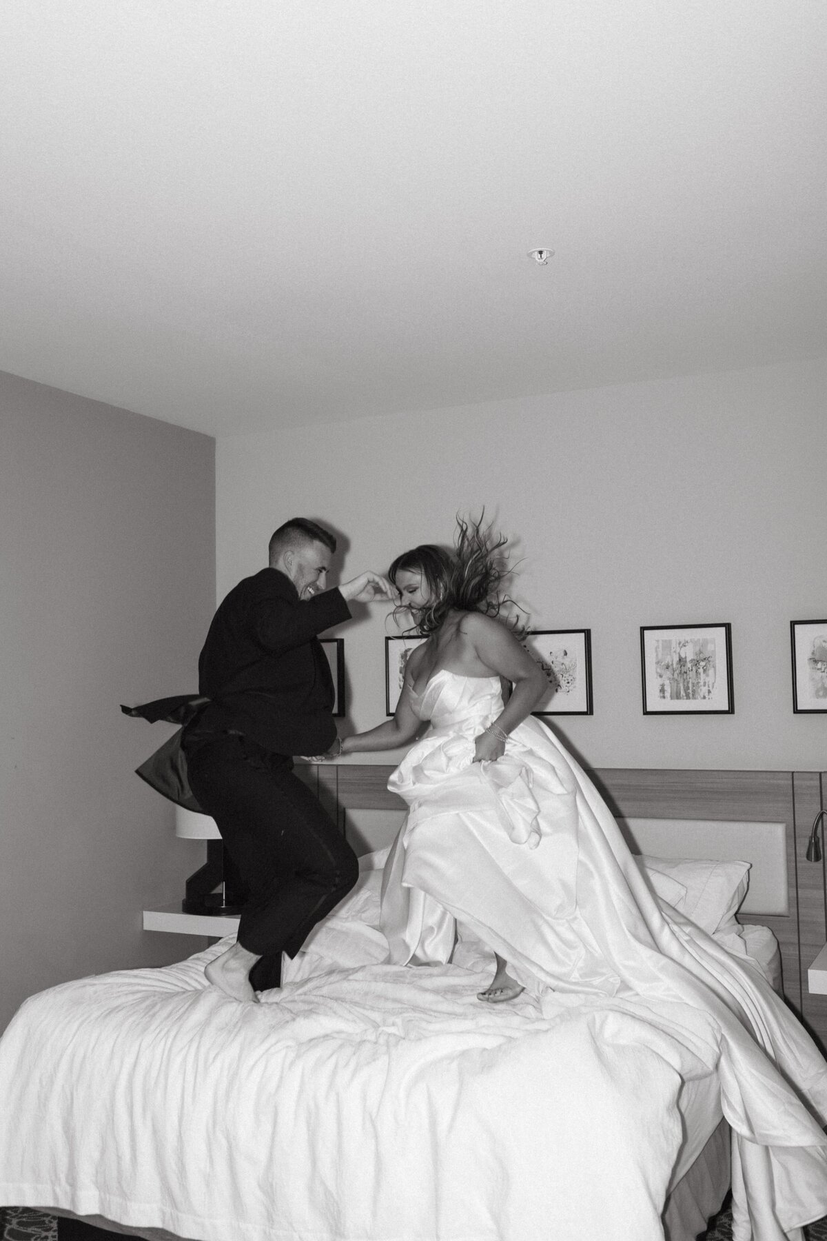 bride and groom jumping on hotel bed