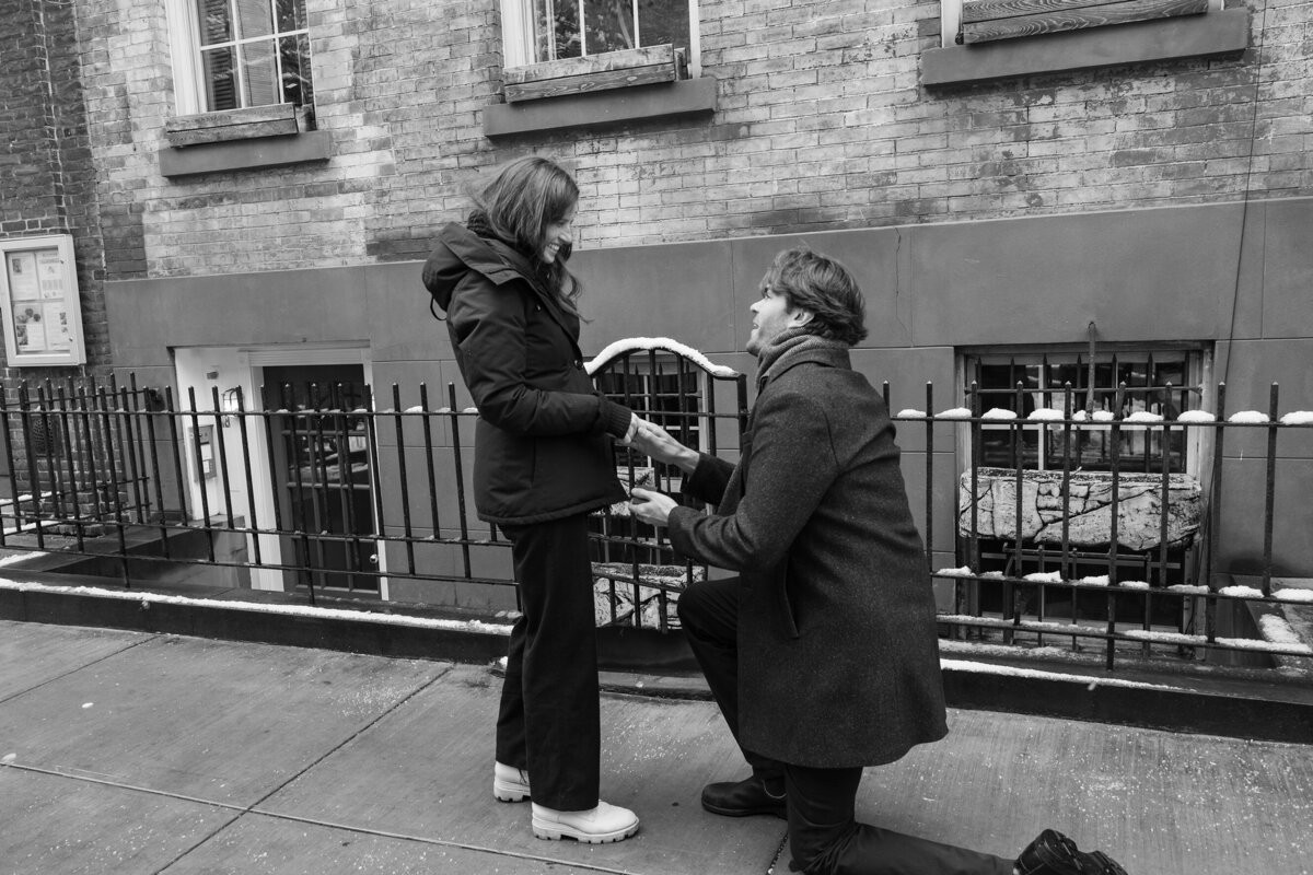 Tall young man kneeling in front of his SOHO townhouse proposing to his girlfriend during winter season.