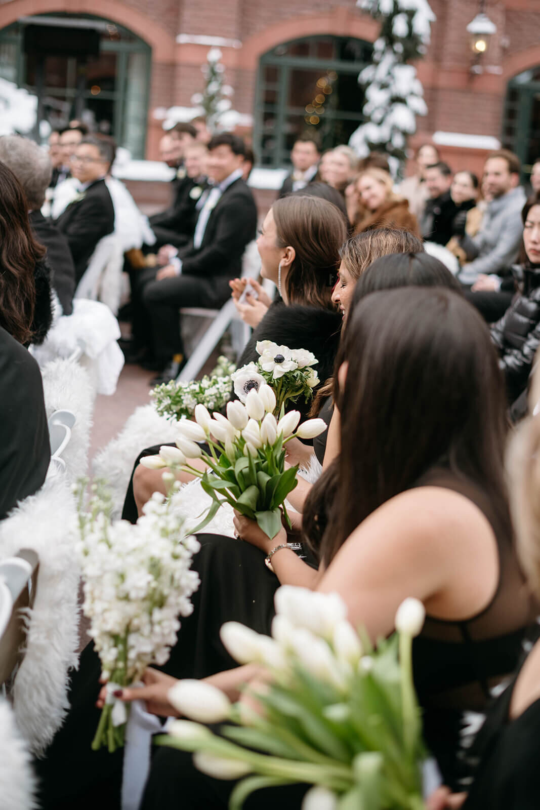 View of the guests attending the outdoor wedding ceremony at Aspen St. Regis featuring white florals against a brick backdrop.