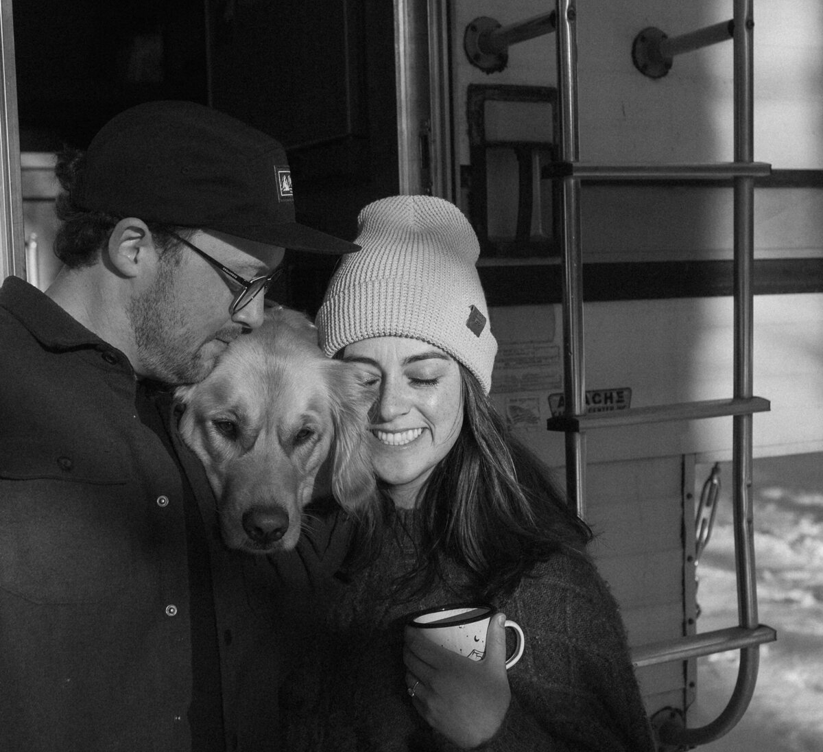 winter engagement couple embracing and sharing an intimate moment with their dog and coffee