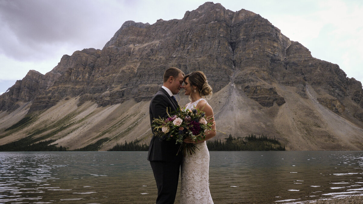 couple standing on the shore of bow lake in banff national park during the filming of their banff elopement video