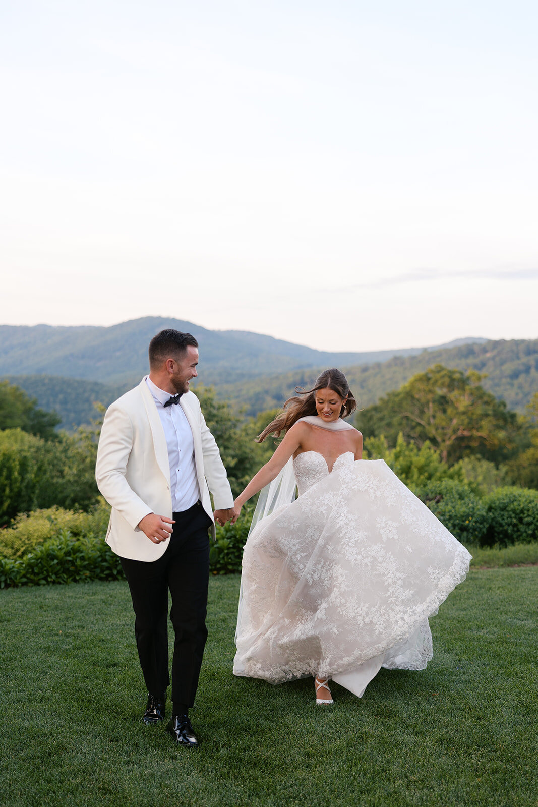  Bride and groom running together with sweeping Blue Ridge Mountain views behind them at a Highlands, NC wedding.