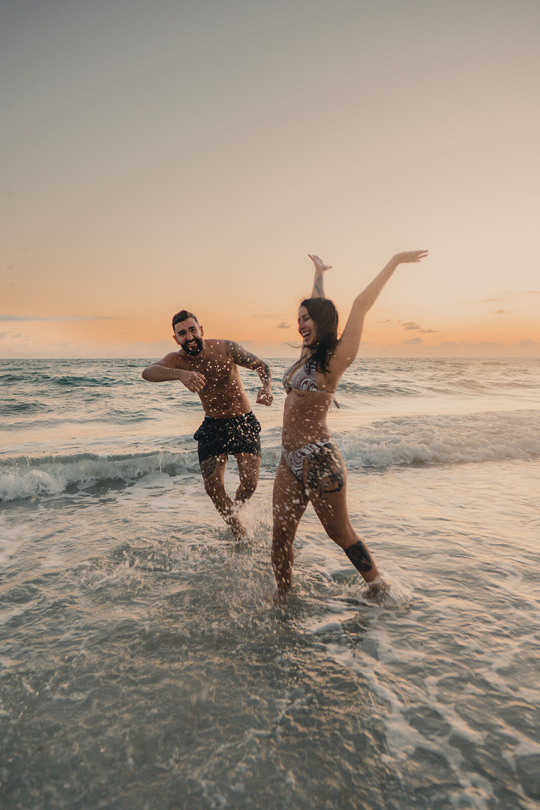 young couple splashing water at beach frolicing running in water