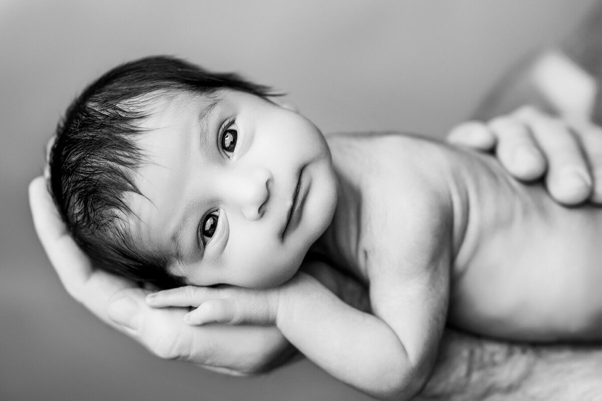 Newborn baby boy with his eyes open being held by dads arm