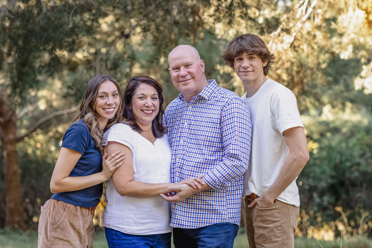 A family of four with brown hair wearing shades of white and blue smiling at the camera at Jeffrey Open Space.