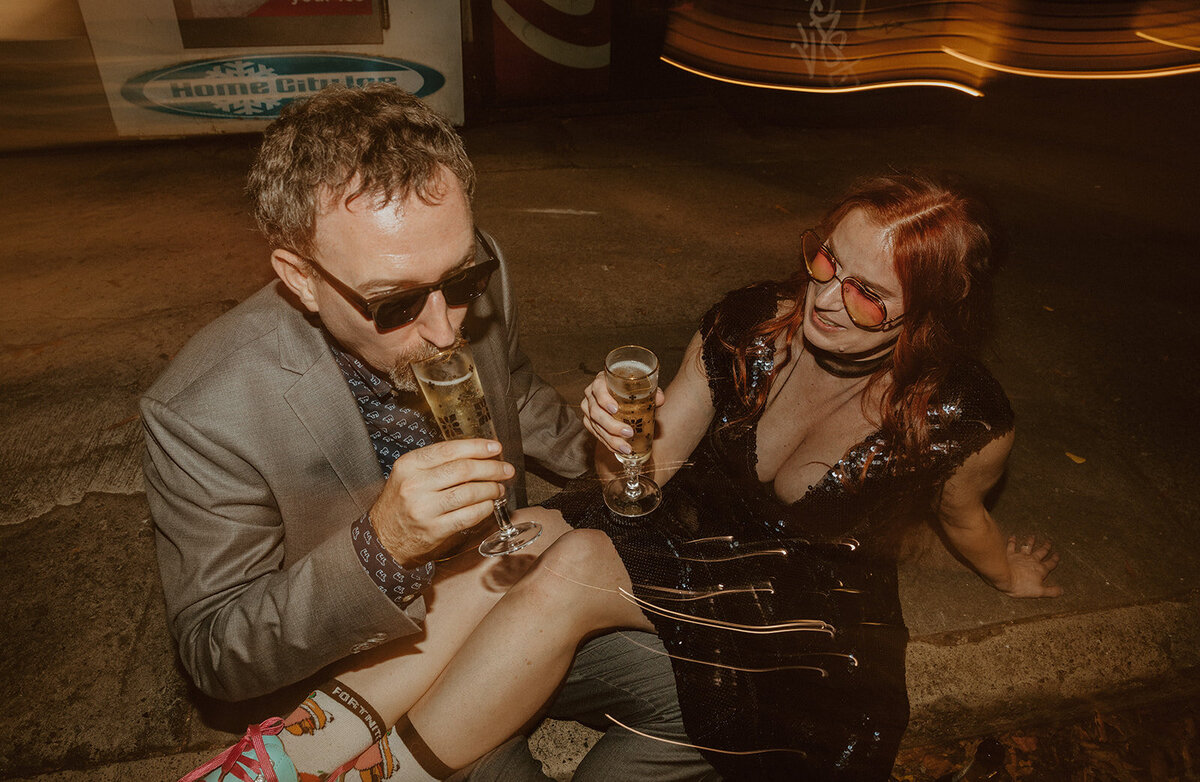 man and woman drinking champagne in street wearing sunglasses and rollerskates