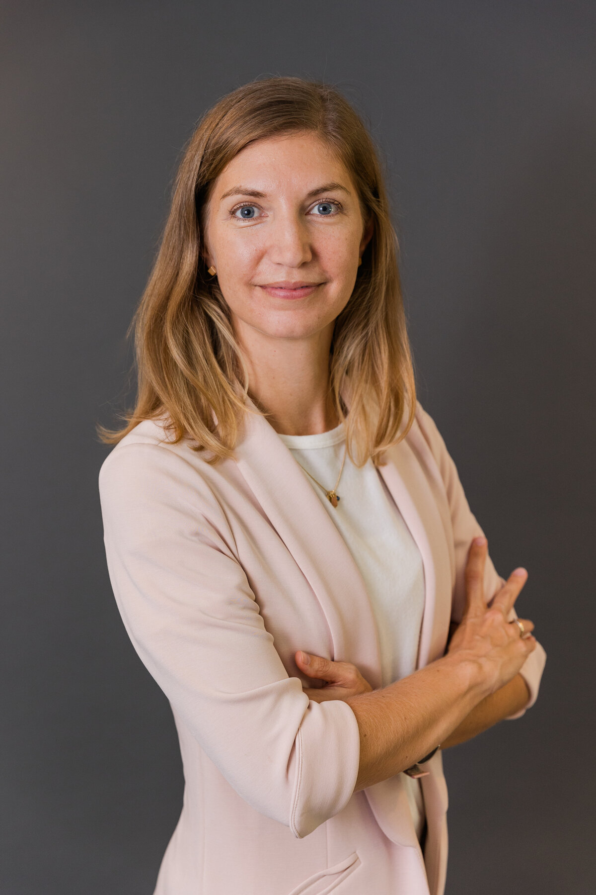 portrait on woman wearing white shirt and light pink jacket arms crossed from the side during photo session