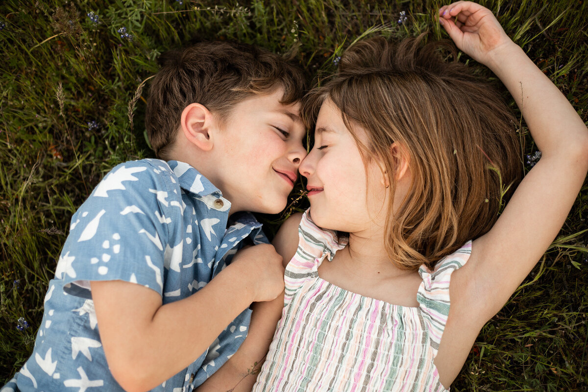 Siblings touching noses while laying in the grass by Portland Oregon family photographer