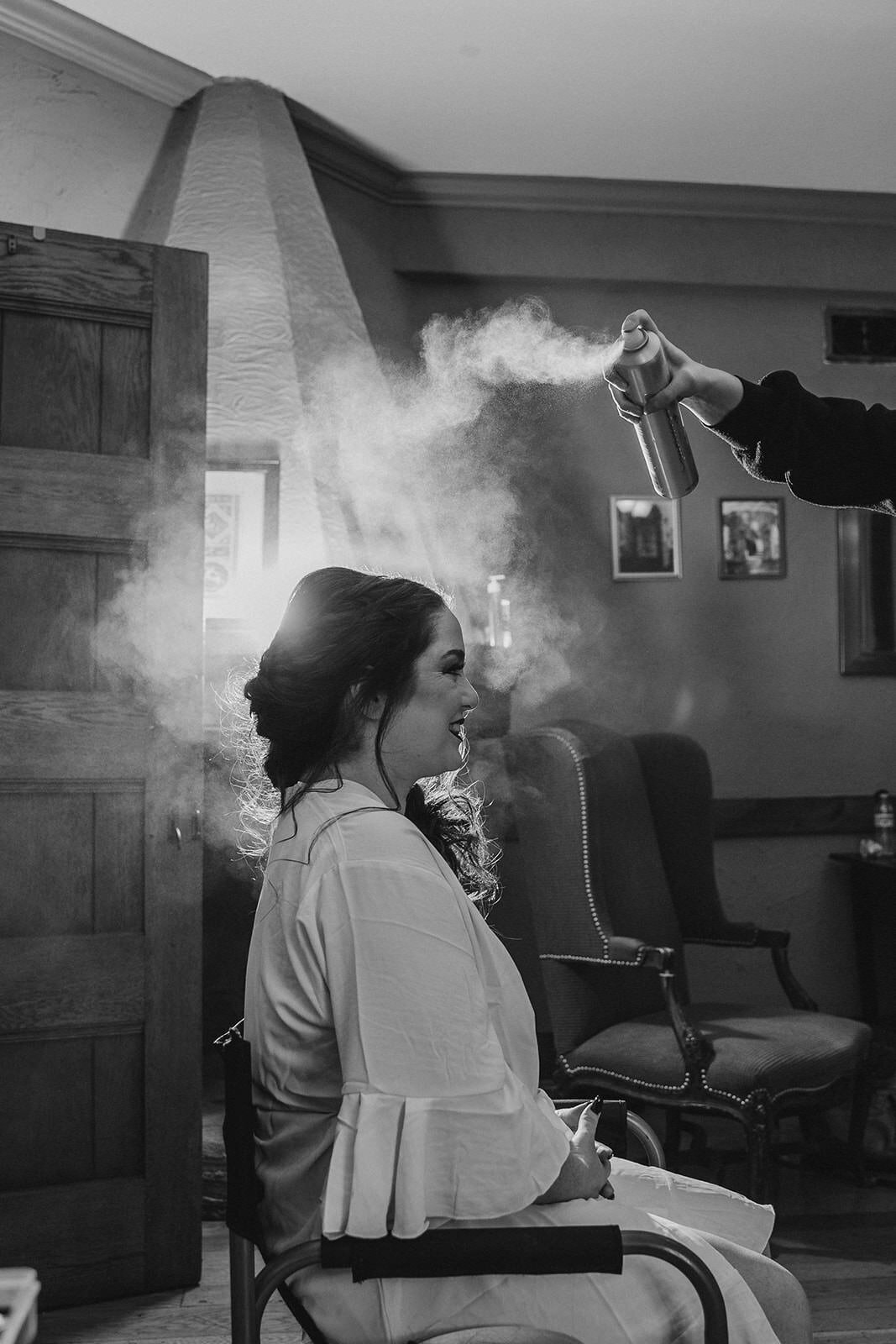 A person sitting down as someone sprays hairspray on them