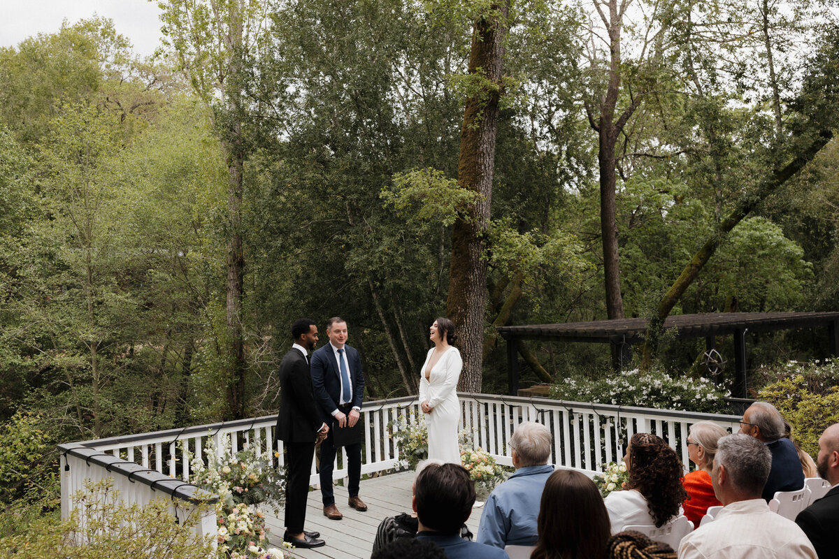 Bride and groom exchanging heartfelt vows on a charming deck surrounded by lush forest. Captured in cinematic style by luxury wedding photographers specializing in authentic, documentary wedding photography.