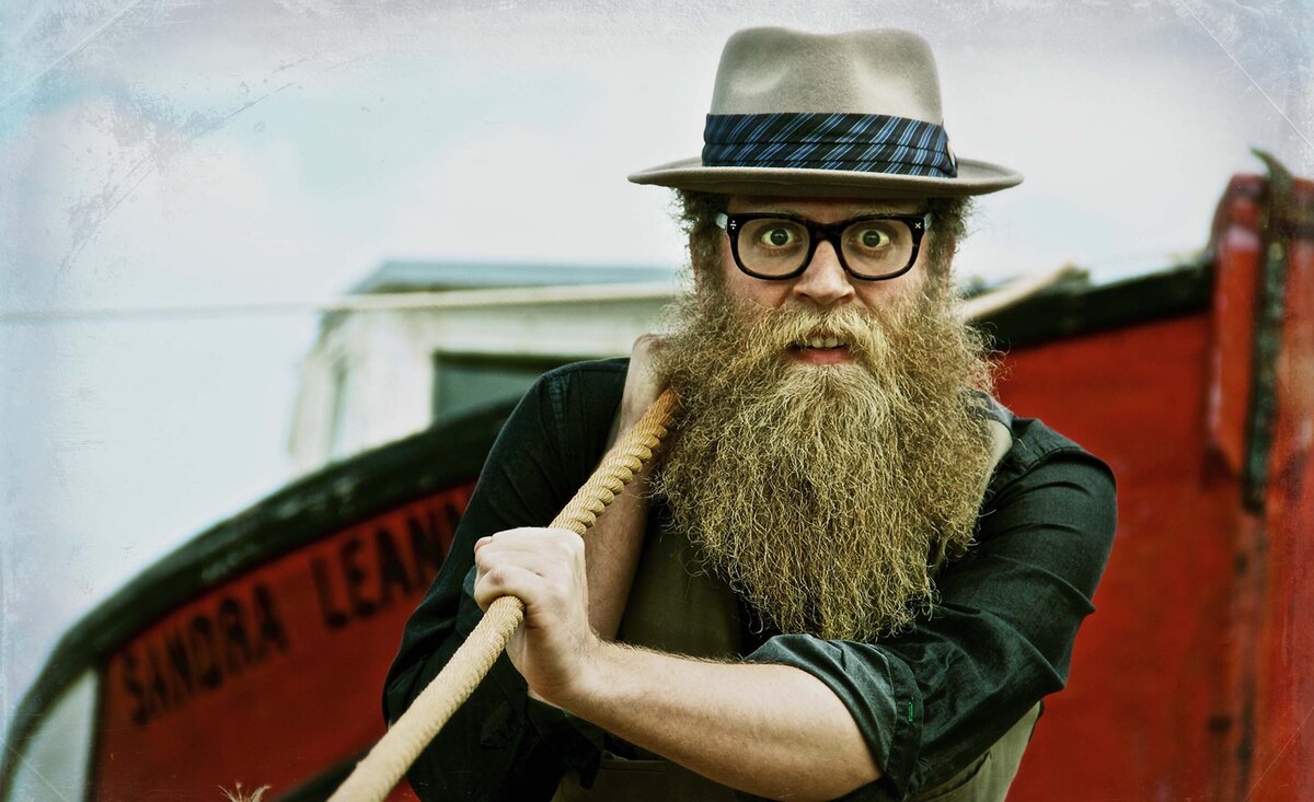Male musician portrait Ben Caplan pulling old fishing boat wearing fedora  with eye glasses