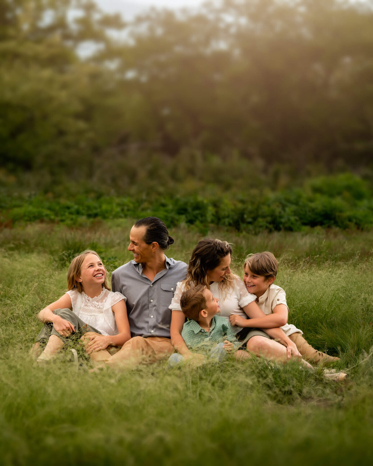 A mom, dad, daughter and two sons snuggling and talking in the grass at Craggy Gardens