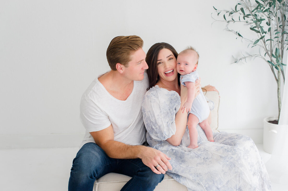 Family wearing gorgeous blues and whites sit on a couch and connect during their newborn session