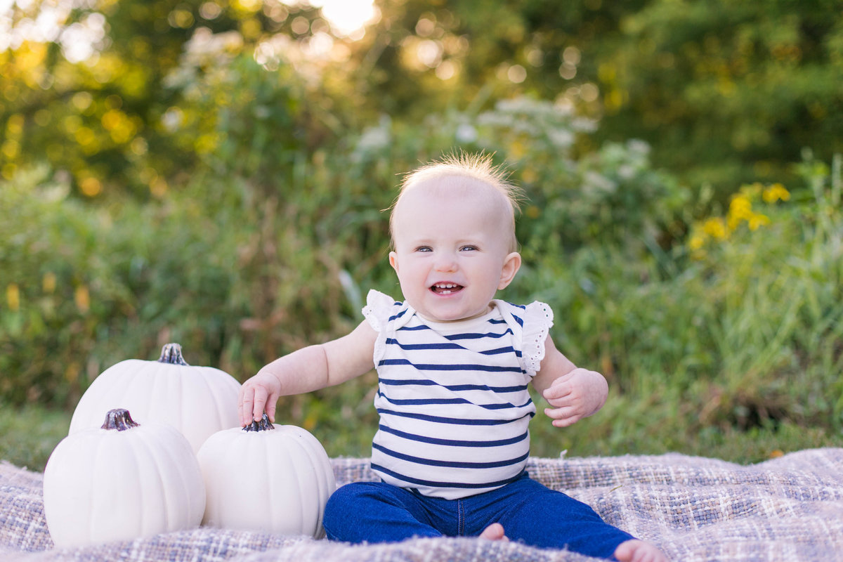 Baby in a field of wildflowers on blanket  with white fall pumpkins